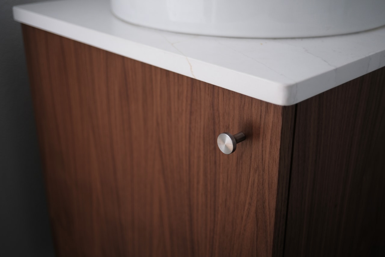 A walnut bathroom vanity door with a small steel knob.