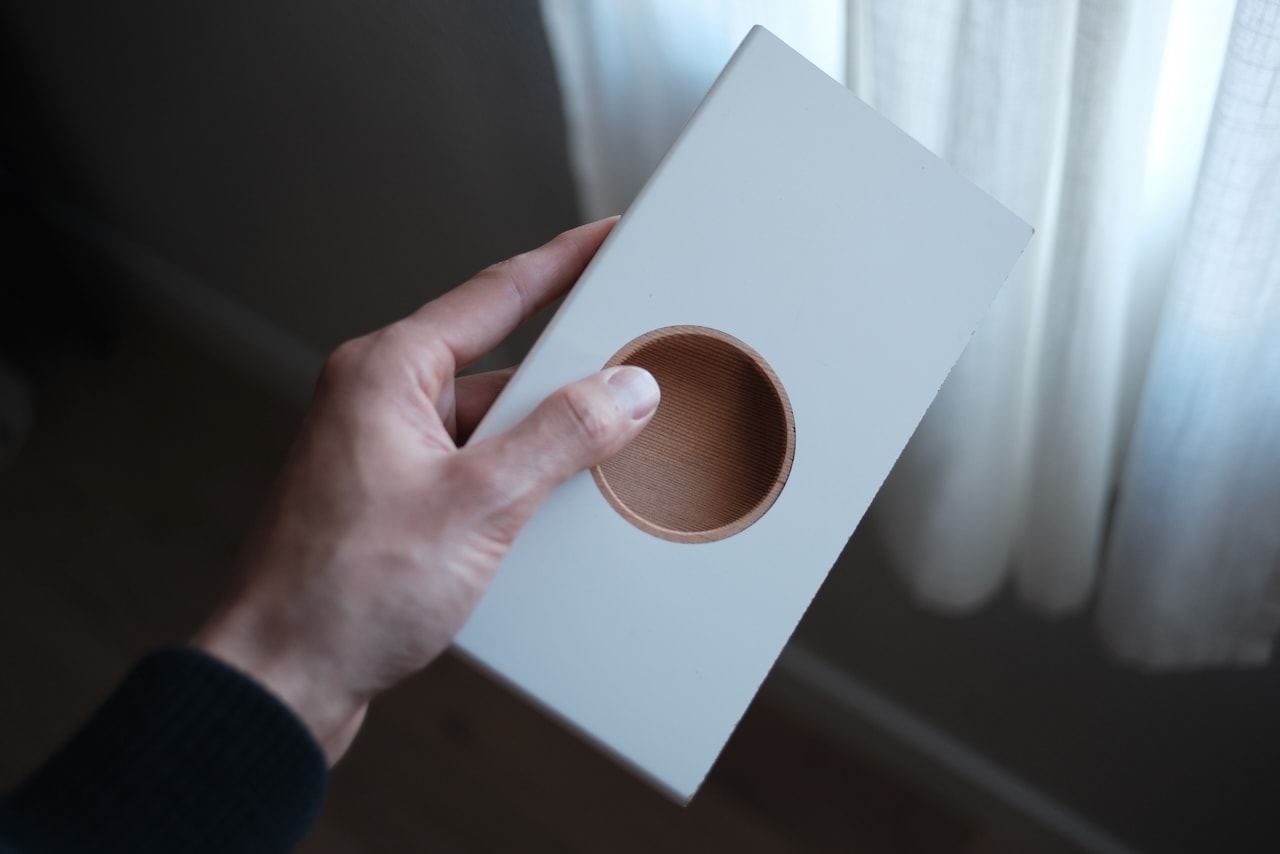 A hand holding a white door with a round, routed finger pull.